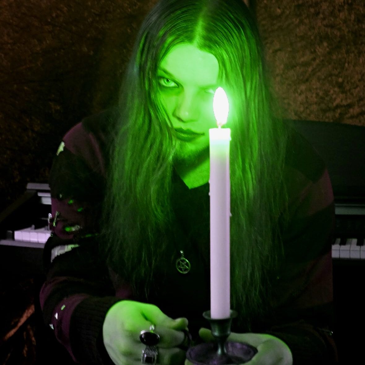 J.U.N.K con una candela in mano, luce verde e atmosfera cupa.